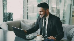 Man looking and smiling at computer with a coffee